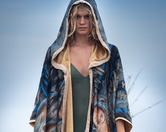 May include: A woman wearing a hooded, blue, gold, and black patterned cape with a green dress underneath. The cape has a gold trim and a floral design.