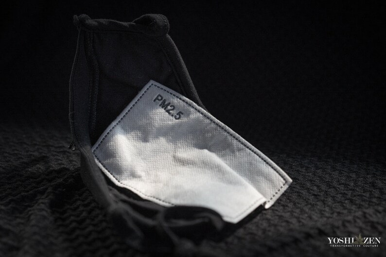 May include: A black face mask with a white PM2.5 filter insert. The filter is visible through the fabric of the mask.