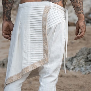 K&ouml;nnte beinhalten: Wei&szlig;e Leinenhose mit einem Faltendetail und einem braunen Musterbesatz. Die Hose hat eine lockere Passform und eine lange L&auml;nge.