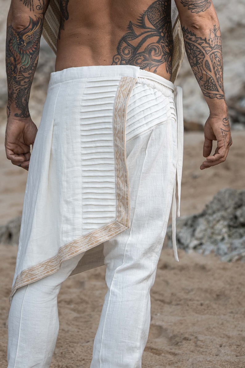 K&ouml;nnte beinhalten: Wei&szlig;e Leinenhose mit einem Faltendetail und einem braunen Musterbesatz. Die Hose hat eine lockere Passform und eine lange L&auml;nge.