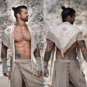 May include: A person wearing a white crocheted shawl with a geometric design. The shawl is tied around the neck and hangs down the front of the body. The person is wearing beige pants with a decorative waistband.