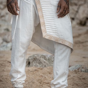 K&ouml;nnte beinhalten: Wei&szlig;e Hose mit dekorativem goldenen Besatz und einem einzigartigen Design. Die Hose ist locker geschnitten und hat einen Kordelzug in der Taille.