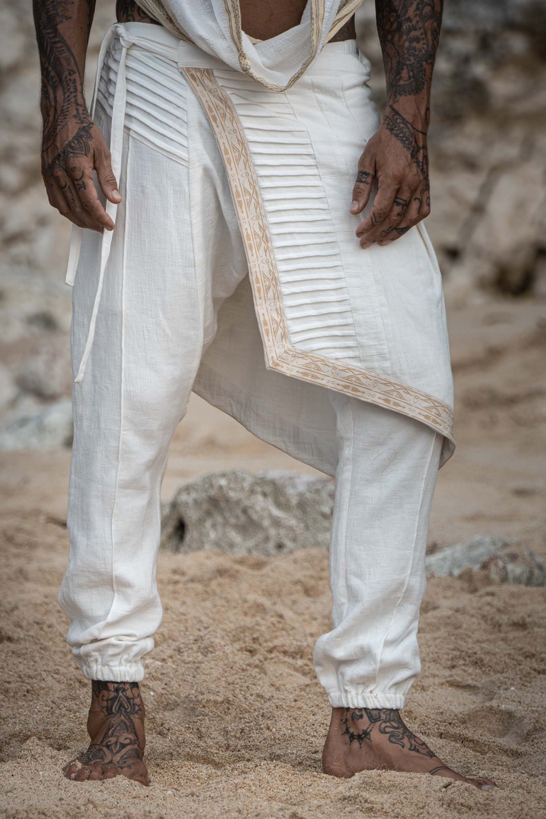 K&ouml;nnte beinhalten: Wei&szlig;e Hose mit dekorativem goldenen Besatz und einem einzigartigen Design. Die Hose ist locker geschnitten und hat einen Kordelzug in der Taille.