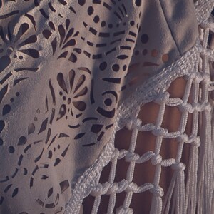 May include: White crochet top with a delicate lace pattern and fringe detail. The top is made of a lightweight fabric and has a relaxed fit.