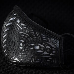 May include: A black face mask with a silver geometric pattern. The mask is made of a soft, breathable fabric and has a comfortable fit.