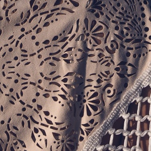 May include: A white crocheted top with a delicate floral pattern and a fringe trim. The top features a cut-out design and a logo on the front.