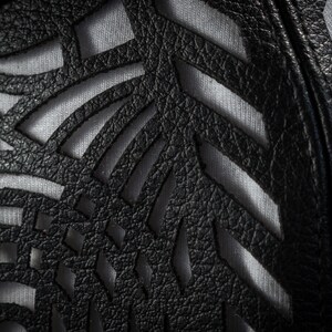 May include: Close-up of a black leather fabric with a cut-out design. The fabric has a textured surface and is layered over a white fabric.