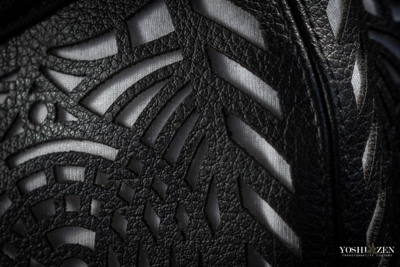 May include: Close-up of a black leather fabric with a cut-out design. The fabric has a textured surface and is layered over a white fabric.