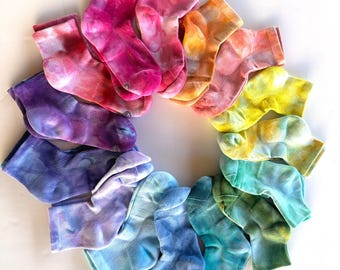 May include: A circular arrangement of tie-dye socks in various colors, including pink, orange, yellow, green, blue, and purple. The socks are arranged on a white surface, showcasing the vibrant patterns and hues of the fabric.