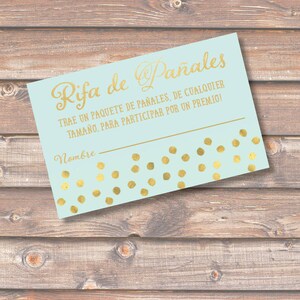 May include: A light blue raffle ticket with gold lettering that reads "Rifa de Pañales" and "TRAE UN PAQUETE DE PAÑALES, DE CUALQUIER TAMAÑO, PARA PARTICIPAR POR UN PREMIO!"  The ticket has a gold polka dot pattern and a blank line for a name.