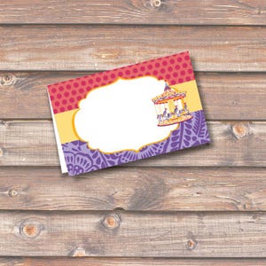 May include: A folded card with a carousel illustration. The card features a white space for text, bordered by a pink polka dot pattern, yellow, and purple floral design. The carousel has yellow, orange, and purple accents.
