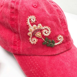 May include: A red baseball cap with an embroidered floral design in shades of pink, orange, and green.