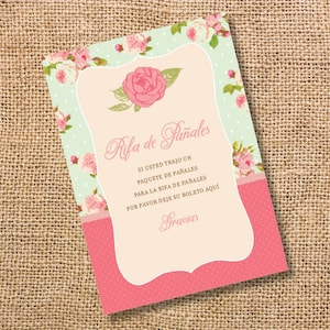 May include: A pink and green floral themed card with the text "Rifa de Pañales" which translates to "Diaper Raffle" in English. The card also includes the text "Si usted trajo un paquete de pañales para la rifa de pañales por favor deje su boleto aquí" which translates to "If you brought a package of diapers for the diaper raffle, please leave your ticket here". The card also includes the word "Gracias" which translates to "Thank you" in English.