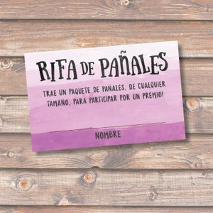 May include: A pink and purple watercolor background with the text "RIFA DE PAÑALES" in black. The text below reads "TRAE UN PAQUETE DE PAÑALES, DE CUALQUIER TAMAÑO, PARA PARTICIPAR POR UN PREMIO!" and "NOMBRE" at the bottom.