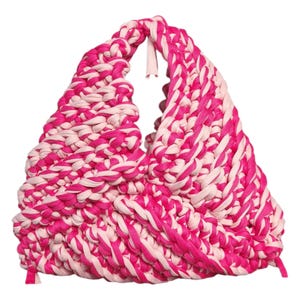 Könnte beinhalten: Eine handgefertigte Tragetasche in Dreiecksform, hergestellt aus dickem, gewebtem Stoff. Die Tasche hat ein auffälliges Farbschema aus leuchtendem Pink und Hellrosa, das ein kühnes und auffälliges Design ergibt. Der Griff ist in die Struktur der Tasche integriert.
