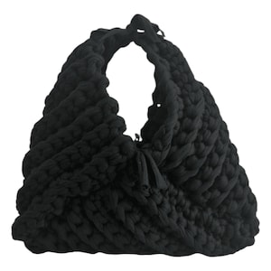 May include: A black, hand-knitted tote bag with a large, open handle. The bag is made of thick, textured yarn, creating a chunky, woven appearance. The bag's design features a knotted closure and a soft, slouchy shape, suitable for carrying various items.