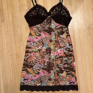 Può includere: Un abito slip marrone con stampa floreale e bordino in pizzo nero. L'abito ha una scollatura a V e spalline sottili.
