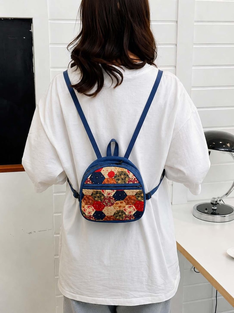 May include: A small blue backpack featuring a front pocket with a multicoloured hexagonal patchwork pattern. The bag has thin blue shoulder straps and a top handle, with a zip closure on the main compartment and the front pocket.