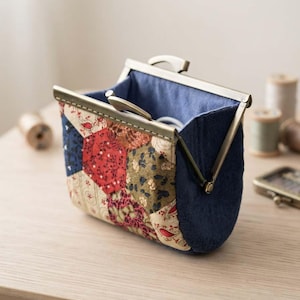 May include: A small pouch with a metal kiss-lock frame. The exterior features a patchwork design of hexagonal fabric pieces in red, olive green, and cream with floral patterns. The sides and interior lining are made of solid dark blue fabric.