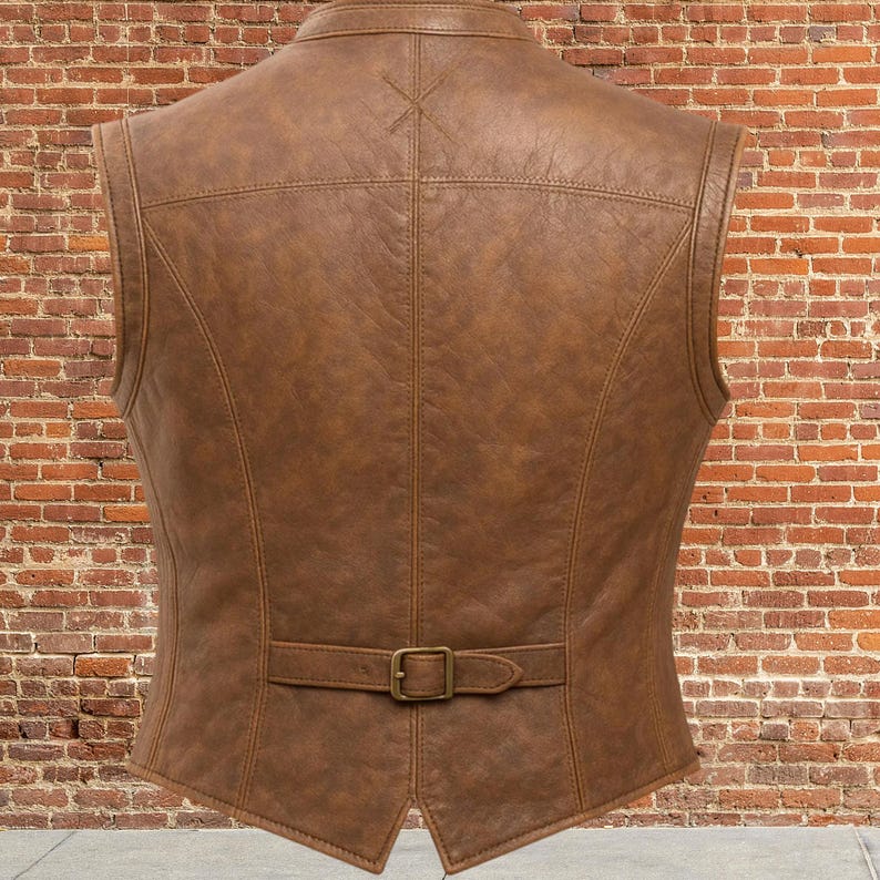 K&ouml;nnte beinhalten: Eine braune Lederweste mit klassischem Design. Die Weste hat einen Reverskragen, einen Schnallenverschluss an der Taille und ein dekoratives Nahtmuster. Die R&uuml;ckseite der Weste ist sichtbar und zeigt die taillierte Passform und die Qualit&auml;t des Leders.