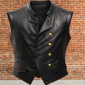 K&ouml;nnte beinhalten: Eine schwarze Lederweste mit Stehkragen und doppelreihigem Design. Die Weste hat vier goldfarbene Kn&ouml;pfe und dekorative Seilverschl&uuml;sse. Zwei kleine Taschen befinden sich an der Taille. Die West ist &auml;rmellos.