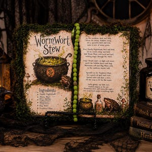 May include: An open book titled Wormwort Stew with moss-covered edges, featuring illustrations of a cauldron, a toad, and a potion bottle. The pages contain a recipe with ingredients like Deadly Nightshade and Frog's Breath, alongside a string of green beads.