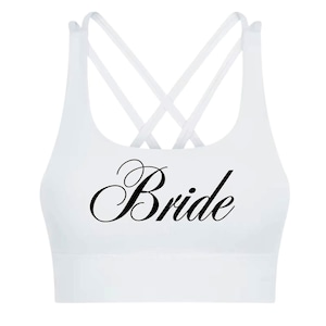 May include: White sports bra with a crisscross back design. The word "Bride" is printed in black script across the front. This athletic top is designed for comfort and support.