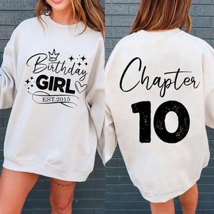Puede incluir: Sudadera color crema con texto negro. La parte delantera dice "Birthday GIRL EST.2015" con una corona, estrellas y un corazón. La parte trasera dice "Chapter 10" en fuente cursiva y números en negrita. Un atuendo casual de cumpleaños.