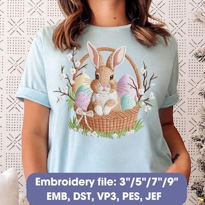 May include: Light blue t-shirt featuring an embroidered Easter design. The design includes a brown bunny in a woven basket with colorful eggs and floral accents. The text "Embroidery file: 3"/5"/7"/9" EMB, DST, VP3, PES, JEF" is at the bottom.