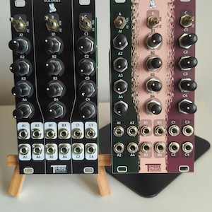 Könnte beinhalten: Zwei modulare Synthesizer-Panels mit der Aufschrift VOLTAGES und TIMBRE INDUSTRIES. Das linke Panel ist schwarz mit drei Kippschaltern, zwölf schwarzen Drehreglern und zwölf Eingangsbuchsen. Das rechte Panel hat grüne, rosa und violette Bereiche mit identischen Bedienelementen.