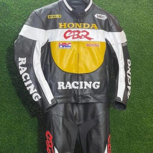 May include: Black and white leather racing suit with yellow and red accents. The suit features the Honda CBR logo, "RACING" text, and sponsor logos. The jacket and pants are designed for motorcycle racing.