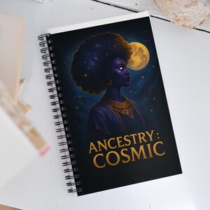 May include: Spiral-bound notebook featuring a celestial illustration of a woman with an afro, set against a starry night sky and a full moon. The text "ANCESTRY: COSMIC" is displayed in gold lettering.
