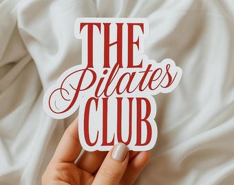 Può includere: Un adesivo bianco con le parole "THE Pilates CLUB" in rosso e in corsivo. L'adesivo è tenuto in mano su uno sfondo di tessuto bianco. L'adesivo è un prodotto a tema fitness.