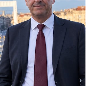 Peut inclure: Une personne d'&acirc;ge m&ucirc;r aux cheveux courts et fonc&eacute;s portant une veste de costume gris anthracite, une chemise blanche &agrave; col rigide et une cravate bordeaux unie. La tenue comprend une ceinture en cuir noir avec une boucle argent&eacute;e sur un pantalon.