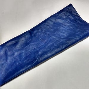 Peut inclure: Une pi&egrave;ce de tissu rectangulaire d'un bleu roi vibrant. Le mat&eacute;riau pr&eacute;sente une surface distincte, l&eacute;g&egrave;rement froiss&eacute;e et textur&eacute;e qui capte la lumi&egrave;re, cr&eacute;ant des variations de tons subtiles sur toute la surface lisse et pli&eacute;e.