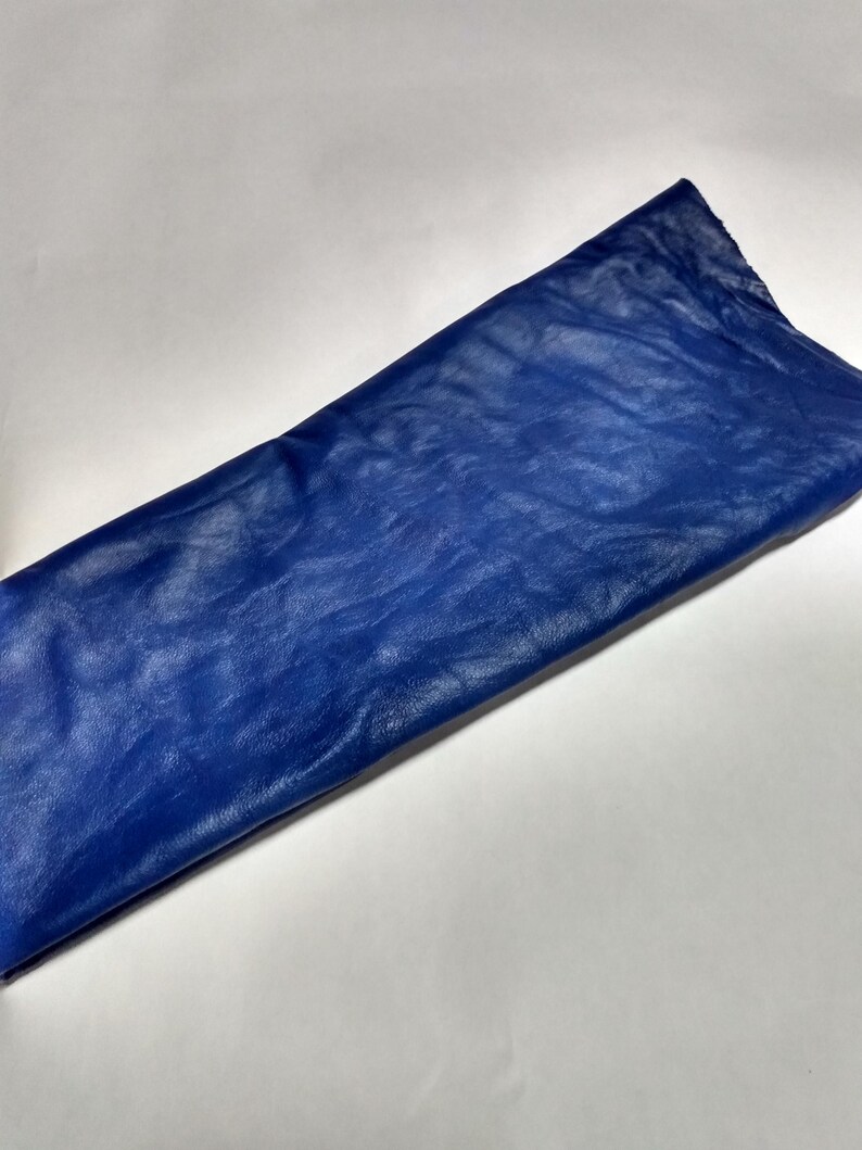 Peut inclure: Une pi&egrave;ce de tissu rectangulaire d'un bleu roi vibrant. Le mat&eacute;riau pr&eacute;sente une surface distincte, l&eacute;g&egrave;rement froiss&eacute;e et textur&eacute;e qui capte la lumi&egrave;re, cr&eacute;ant des variations de tons subtiles sur toute la surface lisse et pli&eacute;e.