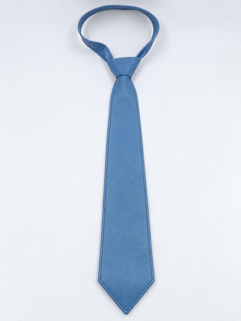 Peut inclure: Une cravate bleu clair unie dot&eacute;e d'une texture lisse et mate avec une extr&eacute;mit&eacute; pointue. La cravate pr&eacute;sente des coutures ton sur ton visibles le long des bords et comprend un n&oelig;ud pr&eacute;-nou&eacute; avec une boucle de cou r&eacute;glable pour la fixation.