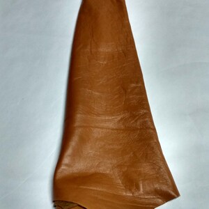 Peut inclure: Une pi&egrave;ce unique de cuir de couleur havane pli&eacute;e en forme triangulaire. La surface du cuir pr&eacute;sente une texture &agrave; grain naturel avec des plis et des ondulations subtils sur toute la mati&egrave;re, r&eacute;v&eacute;lant une finition lisse sur le dessus.