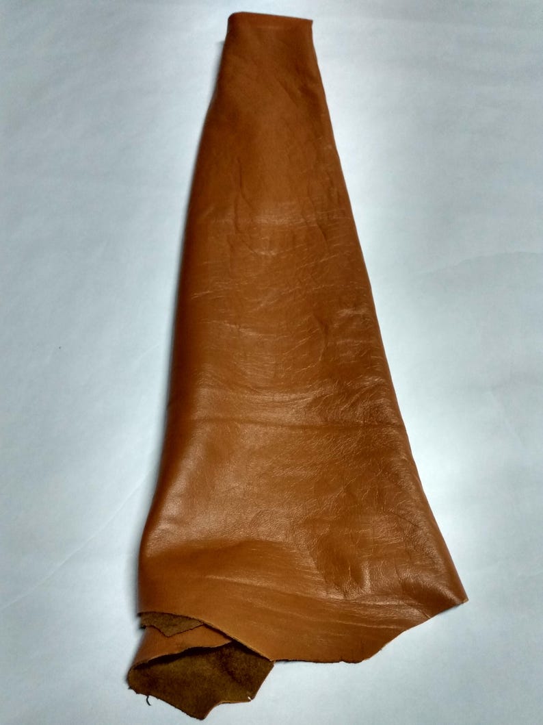Peut inclure: Une pi&egrave;ce unique de cuir de couleur havane pli&eacute;e en forme triangulaire. La surface du cuir pr&eacute;sente une texture &agrave; grain naturel avec des plis et des ondulations subtils sur toute la mati&egrave;re, r&eacute;v&eacute;lant une finition lisse sur le dessus.