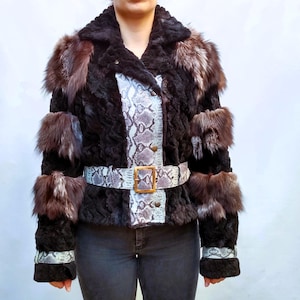 May include: A black fur jacket with brown fur accents on the shoulders and sleeves. The jacket features a snakeskin-patterned panel down the front and a matching belt with a gold buckle. The jacket is worn over dark jeans.