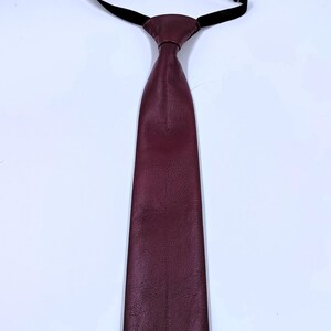 Peut inclure: Une cravate bordeaux fonc&eacute; avec une surface textur&eacute;e et une extr&eacute;mit&eacute; pointue. La cravate pr&eacute;sente un n&oelig;ud pr&eacute;-nou&eacute; attach&eacute; &agrave; une fine sangle de cou &eacute;lastique noire r&eacute;glable avec une boucle coulissante en m&eacute;tal argent&eacute; pour l'ajustement.