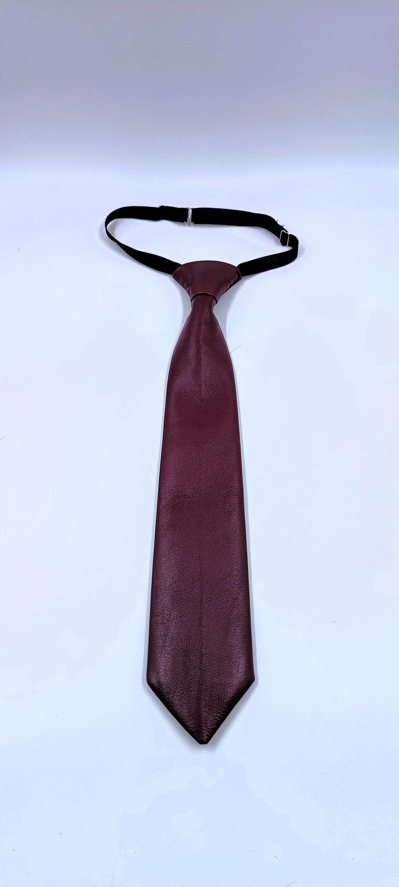 Peut inclure: Une cravate bordeaux fonc&eacute; avec une surface textur&eacute;e et une extr&eacute;mit&eacute; pointue. La cravate pr&eacute;sente un n&oelig;ud pr&eacute;-nou&eacute; attach&eacute; &agrave; une fine sangle de cou &eacute;lastique noire r&eacute;glable avec une boucle coulissante en m&eacute;tal argent&eacute; pour l'ajustement.