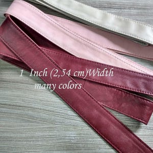 Könnte beinhalten: Drei lange, flache und glatte Streifen in den Farben Weiß, Hellrosa und Dunkelrot. Jeder Streifen hat genähte Kanten und eine Breite von 2,54 cm. Der Text "1 Inch (2,54 cm)Width many colors" ist auf die Streifen gedruckt.