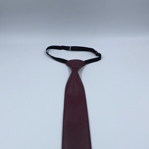 Peut inclure: Une cravate unie de couleur bordeaux fonc&eacute; avec une texture lisse et mate. La cravate pr&eacute;sente un n&oelig;ud pr&eacute;-nou&eacute; et comprend une sangle de cou &eacute;lastique noire r&eacute;glable avec une boucle en m&eacute;tal pour ajuster la longueur autour du col.