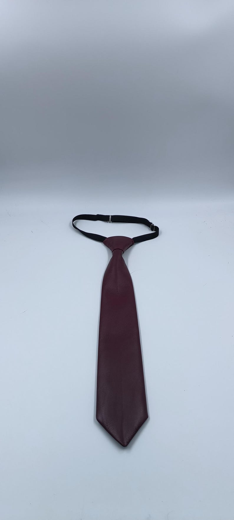 Peut inclure: Une cravate unie de couleur bordeaux fonc&eacute; avec une texture lisse et mate. La cravate pr&eacute;sente un n&oelig;ud pr&eacute;-nou&eacute; et comprend une sangle de cou &eacute;lastique noire r&eacute;glable avec une boucle en m&eacute;tal pour ajuster la longueur autour du col.