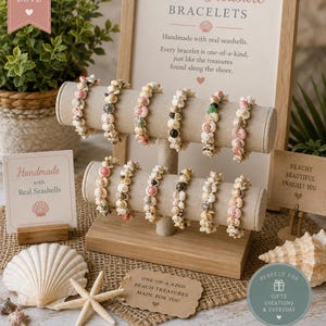 May include: A two-tiered beige fabric display stand holds eleven bracelets crafted from various small, multi-colored seashells. The display includes a sign reading Beach Treasure BRACELETS, along with smaller cards and a starfish on the base.