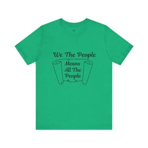 May include: A green t-shirt with the text "We The People Means All The People" in black script. The text is centered on the front of the shirt, above a scroll design.