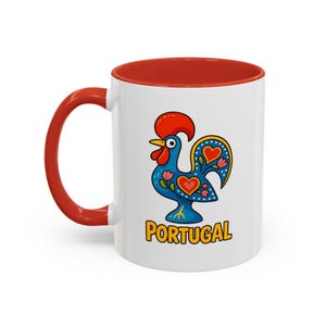 May include: White ceramic mug with a red rim. The mug features a colorful illustration of a rooster with the word "PORTUGAL" printed below it.