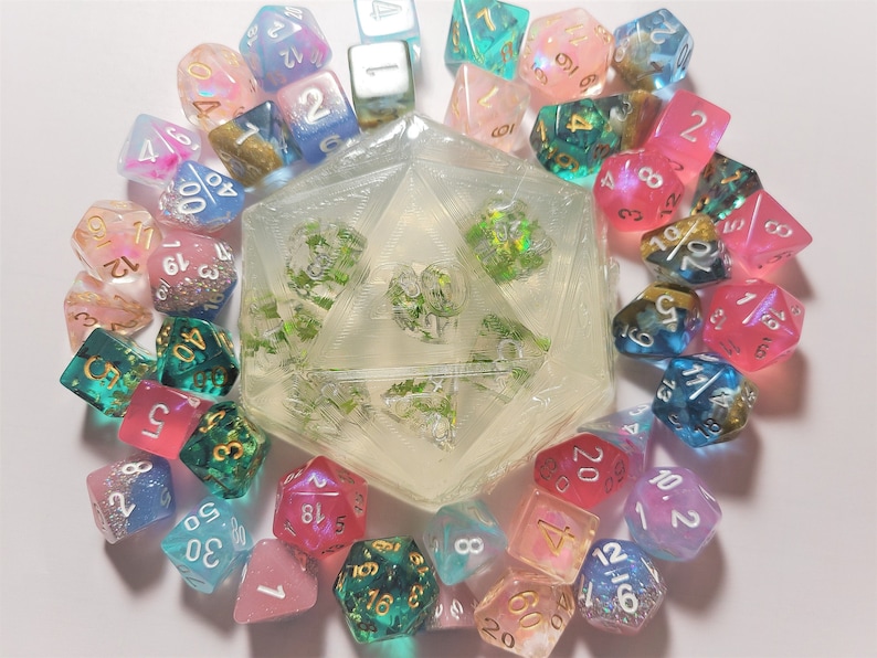 K&ouml;nnte beinhalten: Eine Sammlung von 12-seitigen W&uuml;rfeln in verschiedenen Farben, darunter Pink, Blau, Gr&uuml;n und Wei&szlig;. Die W&uuml;rfel sind aus klarem Harz mit Glitzer und goldenen Akzenten gefertigt. Die W&uuml;rfel sind in einem Kreis um einen gr&ouml;&szlig;eren, klaren Harz-W20 mit gr&uuml;nen Akzenten angeordnet.