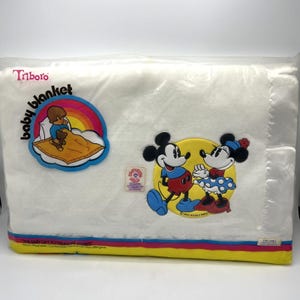 Pu&ograve; includere: Una coperta per bambini bianca in una confezione di plastica. La coperta presenta un design colorato con Topolino e Minnie. La confezione riporta le scritte "baby blanket" e "Triboro".
